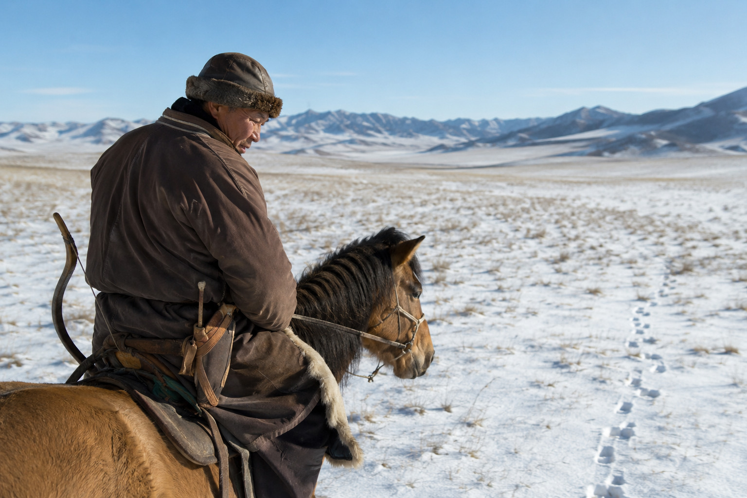 Traditional Hunting in Mongolia: Methods, Ethics and Change 12 A mounted Mongolian hunter observing animal tracks in a snowy steppe landscape with a bow secured at the saddle